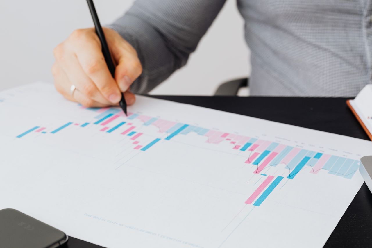 Close-up of a man writing on a printed chart indoors, analyzing colorful data.