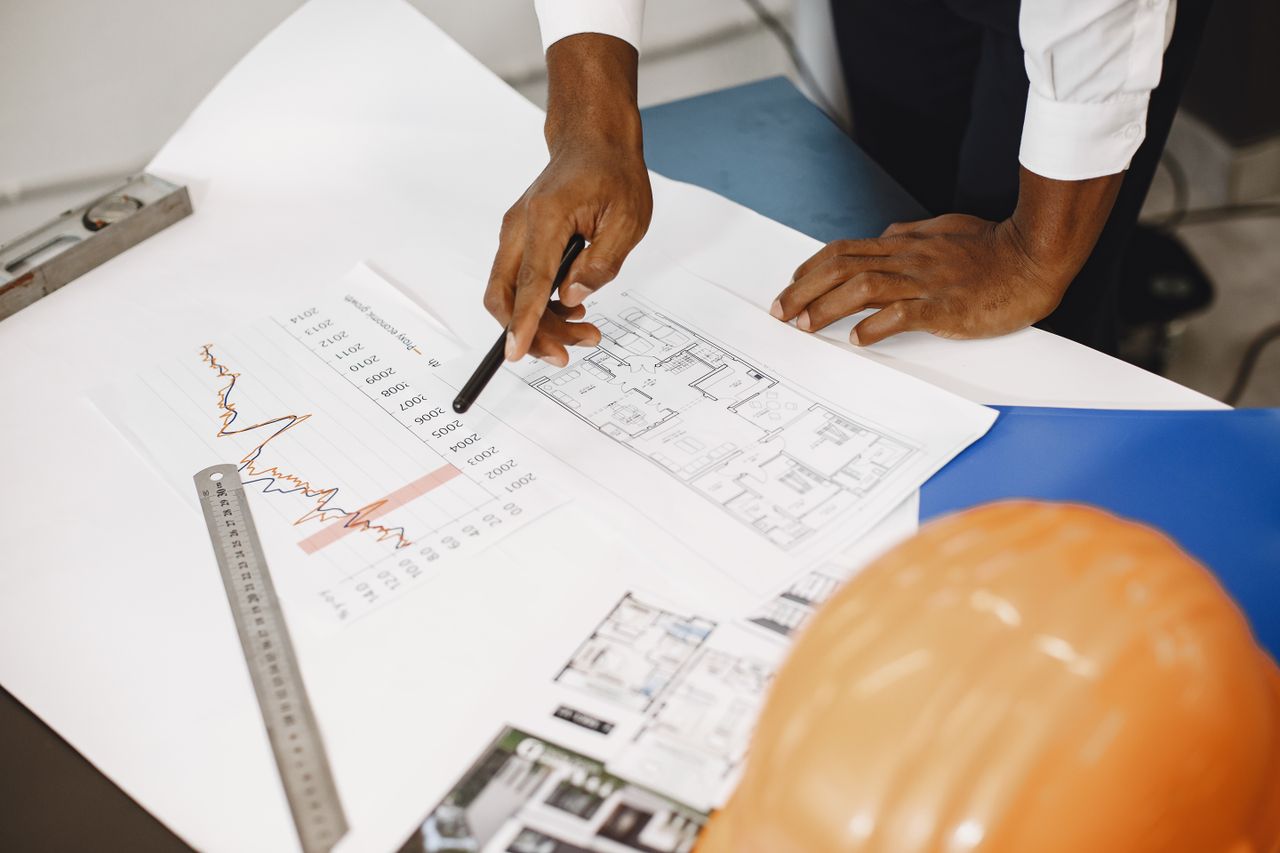 our-experience Hands of an architect analyzing blueprints and financial graphs at a desk.