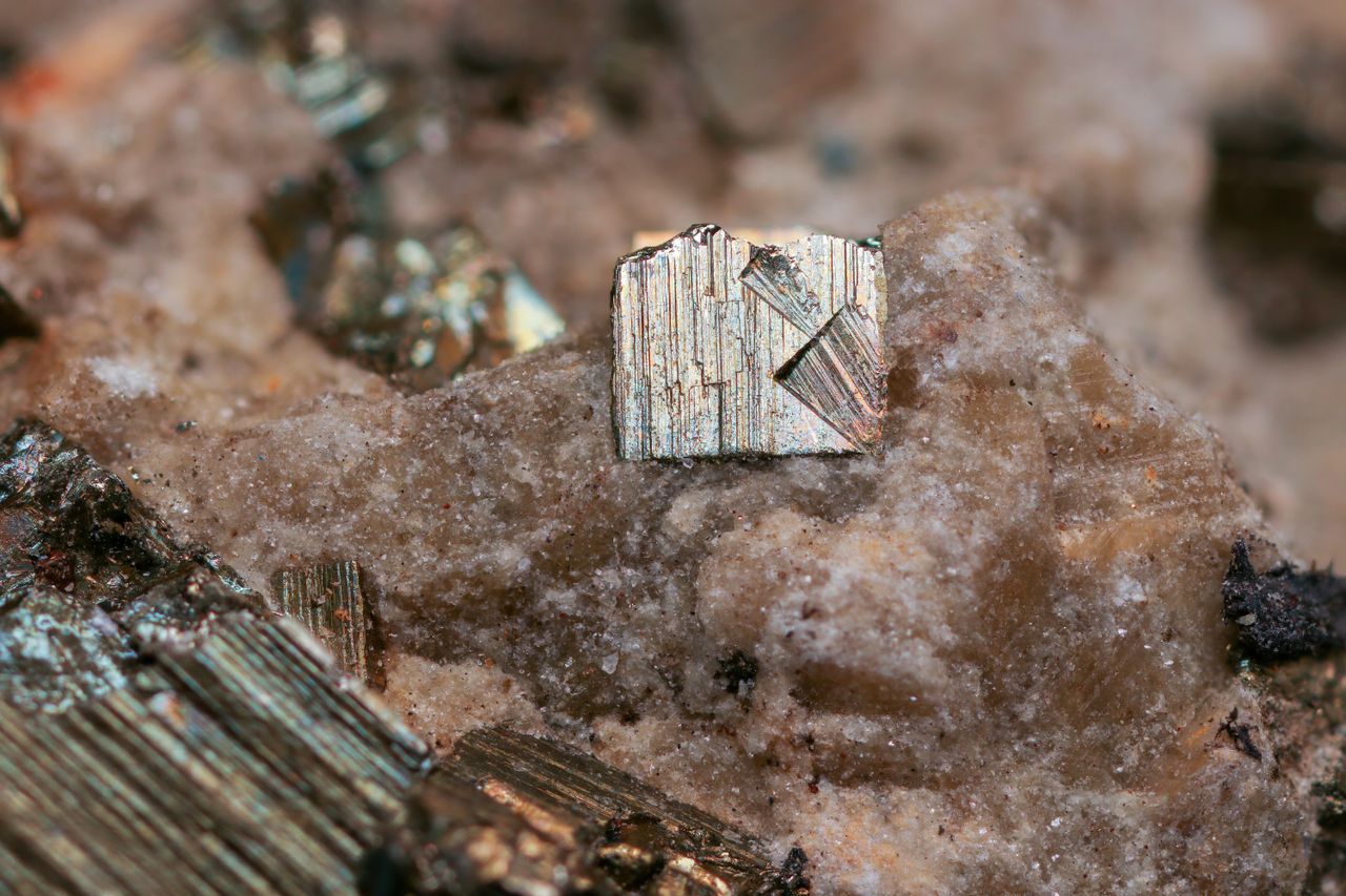 ours-journey Detailed close-up of pyrite crystal on rocky surface, showcasing natural textures and colors.